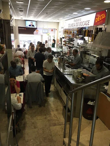 Interior da pastelaria: balcão, mesas e clientes